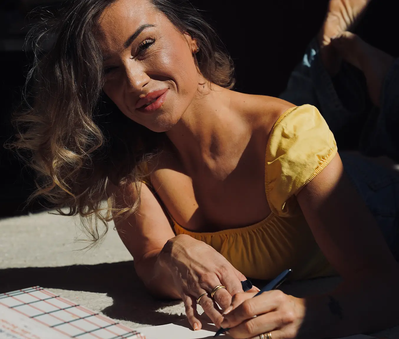 Anna Hahn liegt auf dem Boden, schreibt in ihr Anatomie Journal und lächelt – ein Symbol für Selbstreflexion und achtsame Veränderung.