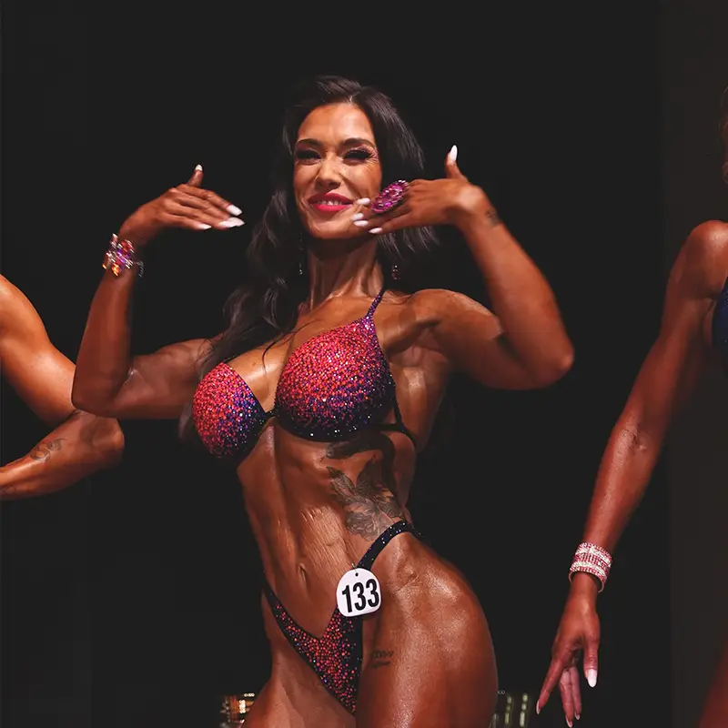 Anna Hahn auf der Bühne bei einem Bodybuilding-Wettkampf – selbstbewusst, durchtrainiert und strahlend im glitzernden Bikini mit Startnummer 133.