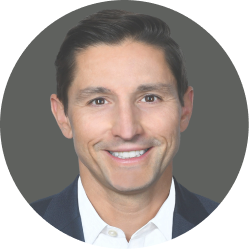 Smiling man with dark hair wearing a white shirt and navy suit jacket against a dark gray background.