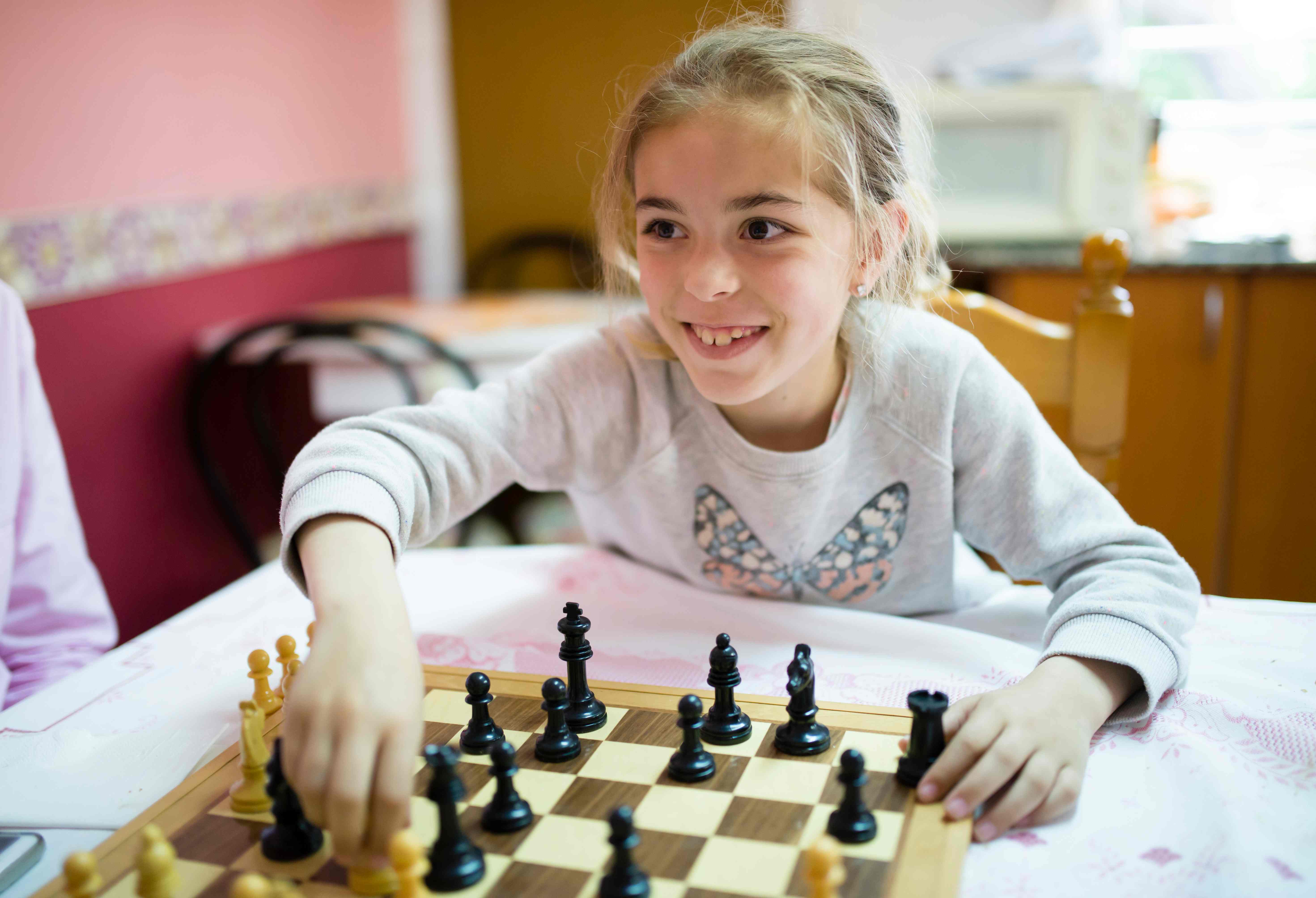 Young, smiling girl playing chess in a family kitchen