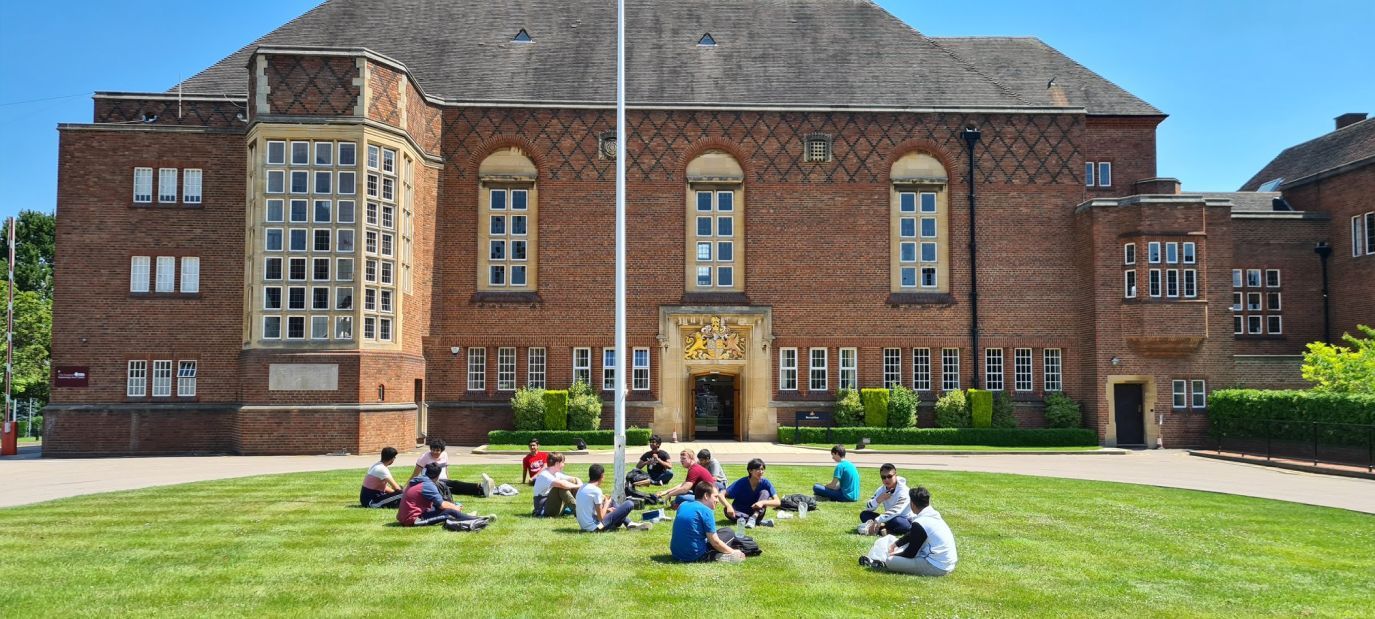 Students sitting on the lawn on a sunny day outside the main entrance building at King Edward's School Birmingham