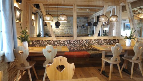 Bergsee mit grünen Hügeln und schneebedeckten Alpen im Hintergrund, zwei Personen sitzen am Ufer.