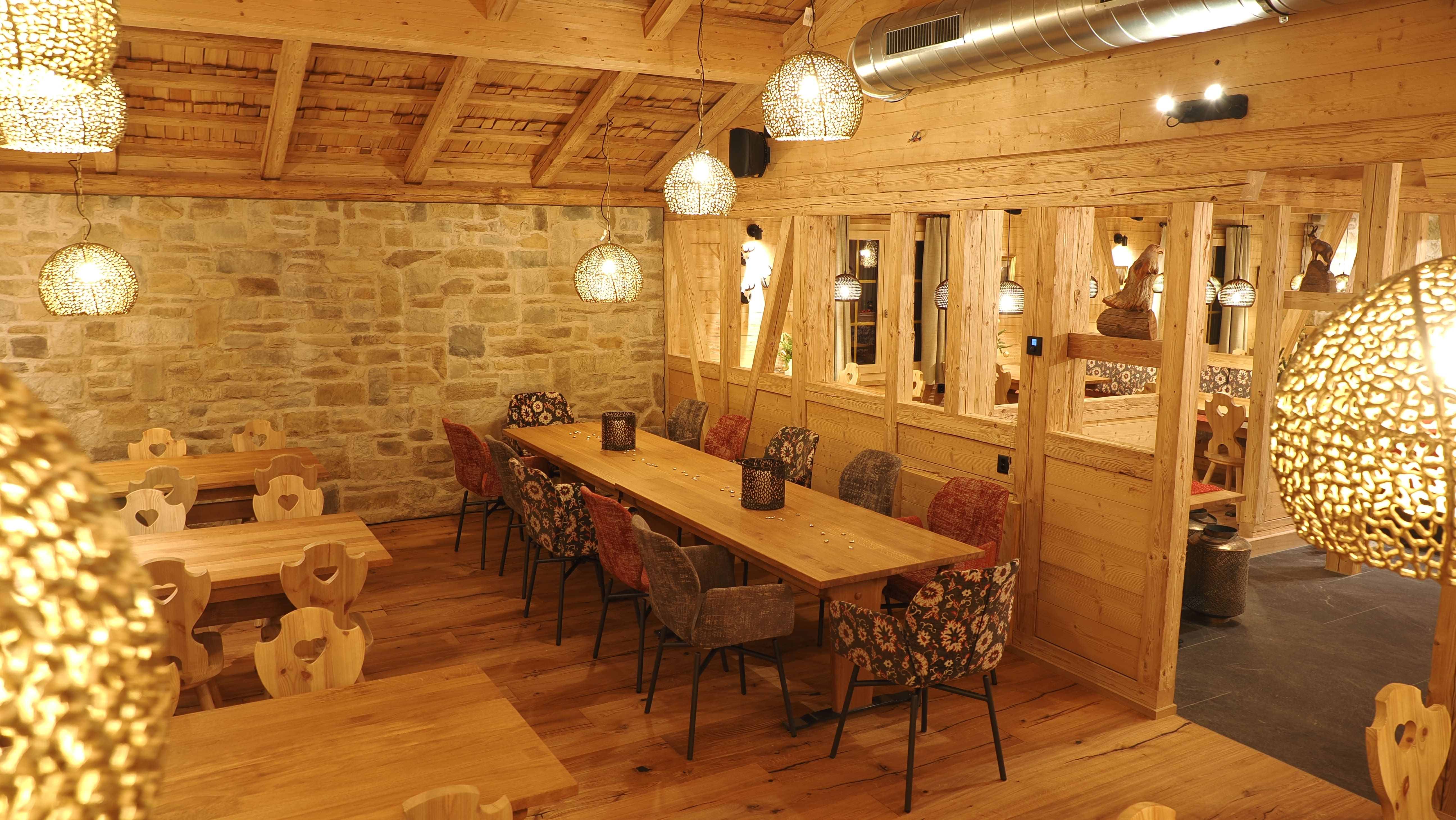 Frau mit Wanderstock führt Kühe mit Glocken und Blumenschmuck auf ihren Hörnern auf einem grasigen Pfad in hügeliger Landschaft.