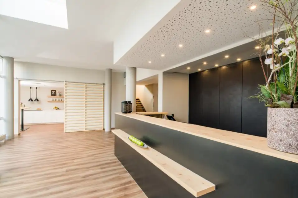 Moderne helle Empfangshalle mit Holzfußboden, langem dunklem Empfangstresen mit hellem Holz, einer Schale mit grünen Äpfeln und einer großen Pflanze.