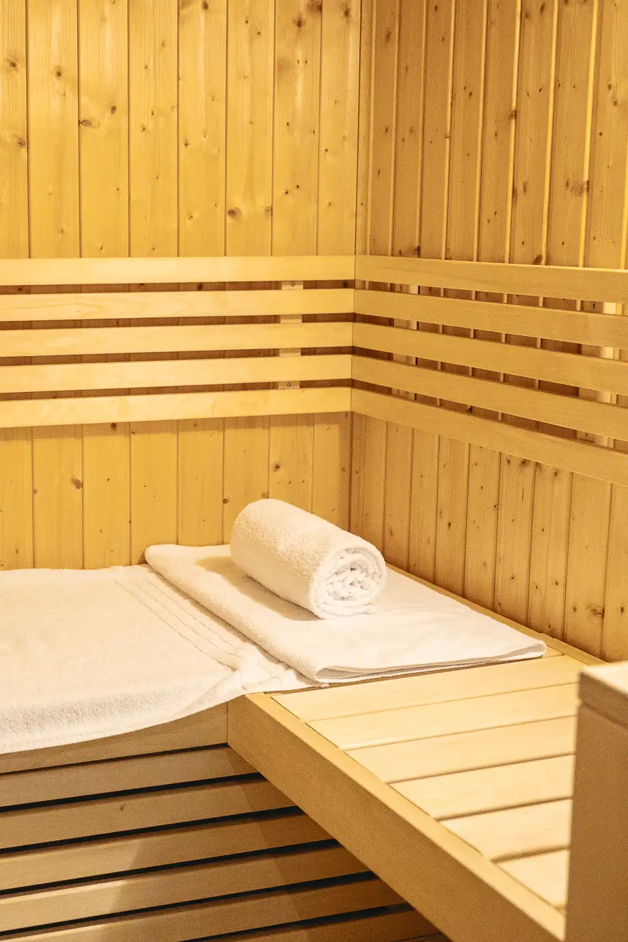 Innenraum einer Sauna mit Holzverkleidung, einer Sitzbank mit weißen Handtüchern, eines davon ist gerollt.