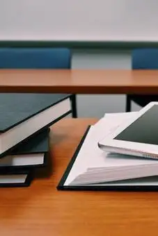 Ein Stapel schwarzer Ordner auf einem Holztisch neben einem aufgeschlagenen Ordner und einem Tablet.