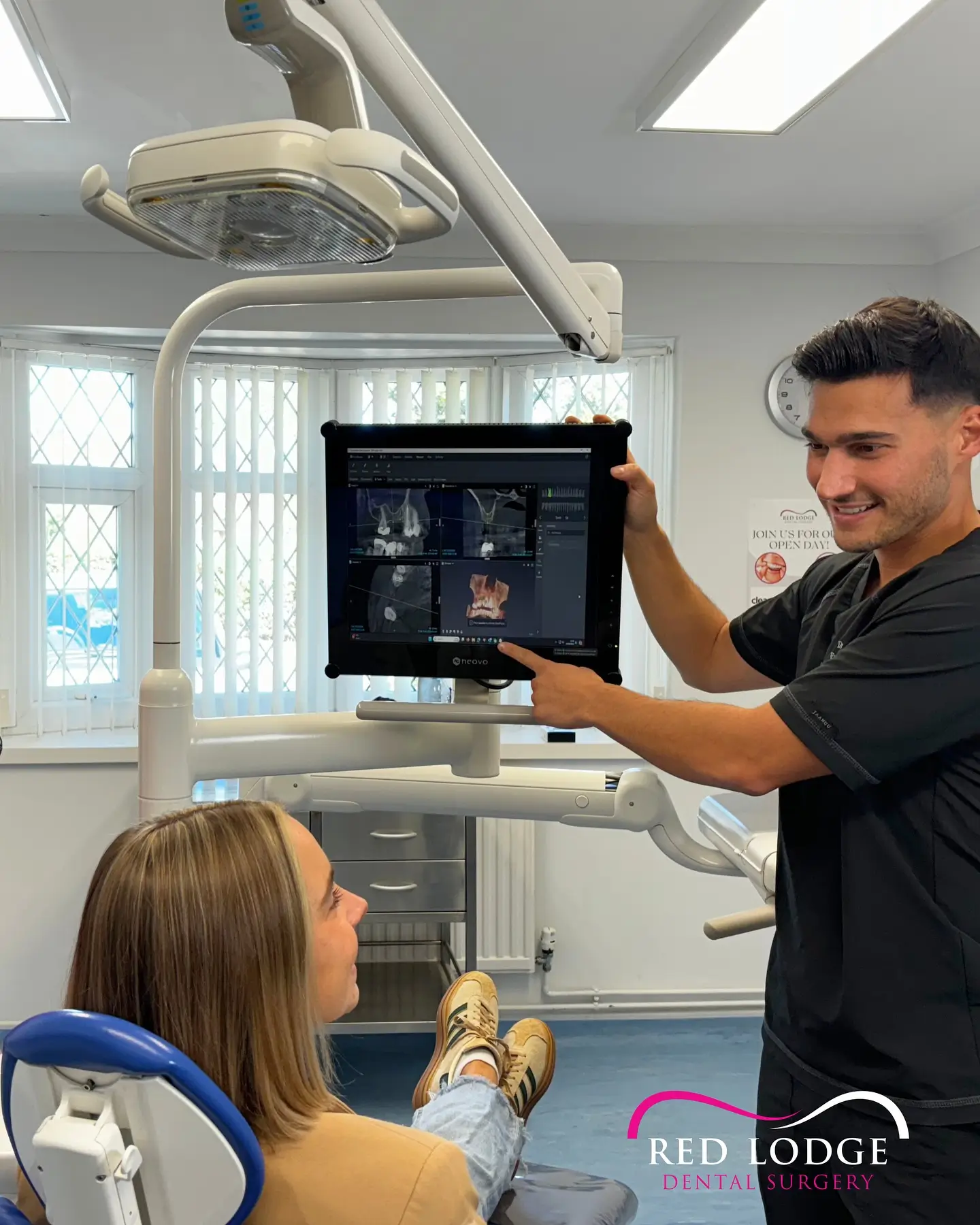 Dentist showing a dental X-ray on a monitor to a seated female patient in a dental clinic.