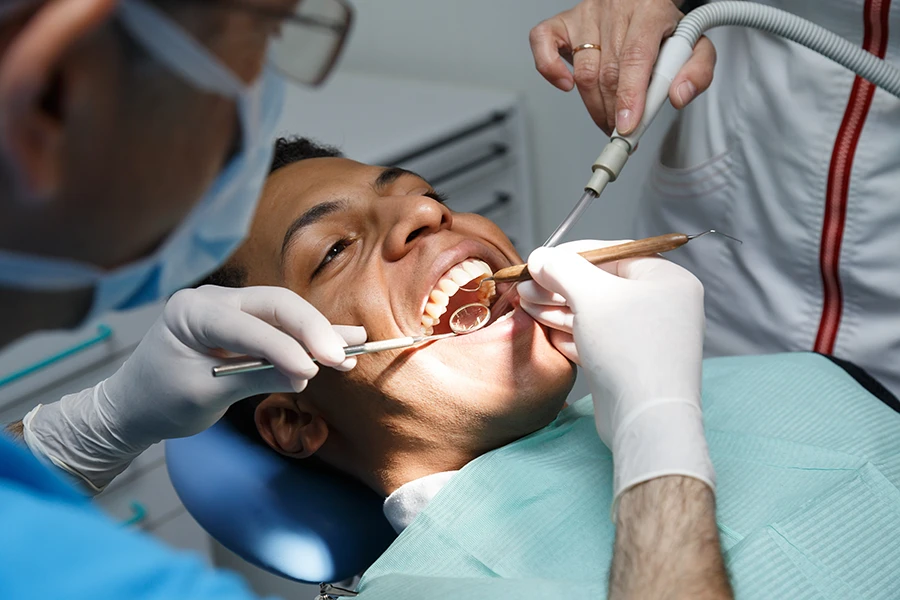 Dentist examining a young male patient's teeth using dental tools and a mirror during a check-up.