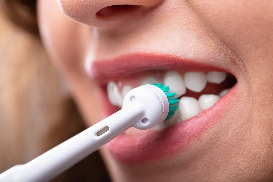 Close-up of a person brushing teeth with a white electric toothbrush head with teal bristles.