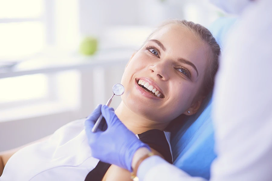 Smiling woman lying in dental chair with dentist holding a dental mirror near her mouth.