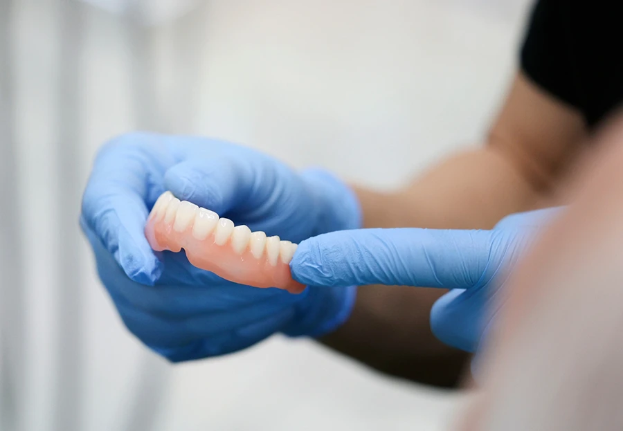 Hands wearing blue gloves holding and pointing at a set of full dentures.