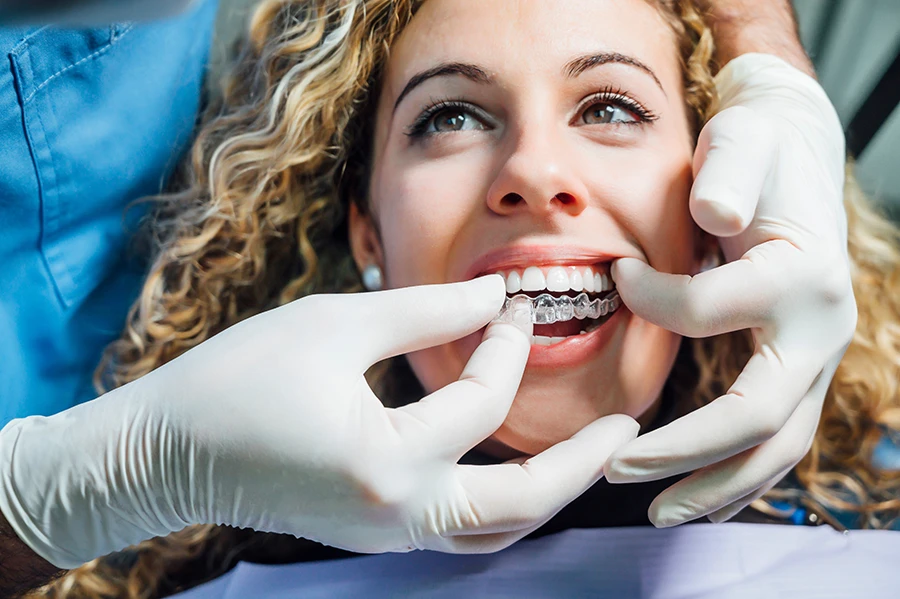 Smiling woman having a clear dental aligner fitted by a gloved dentist.