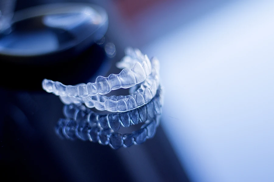 Clear dental aligners placed on a reflective surface with a blurred background.
