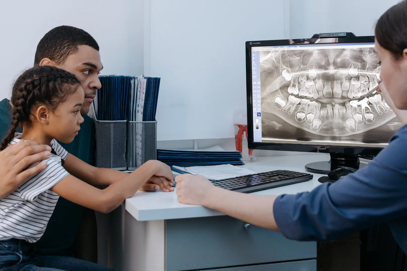 Dentist showing a dental X-ray on a computer screen to a man and a young girl.