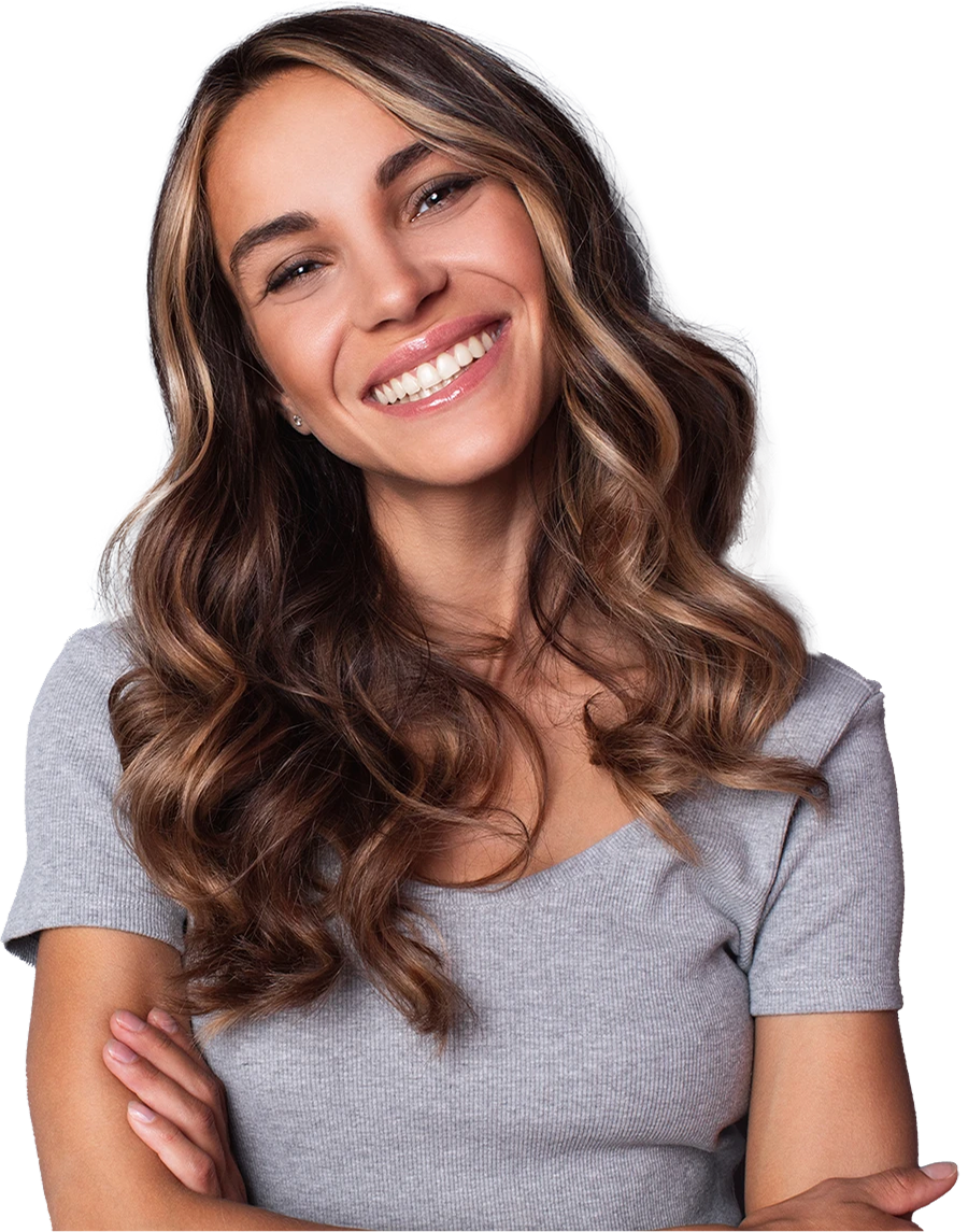 Smiling woman with wavy, highlighted brown hair wearing a light gray short-sleeve top with arms crossed.