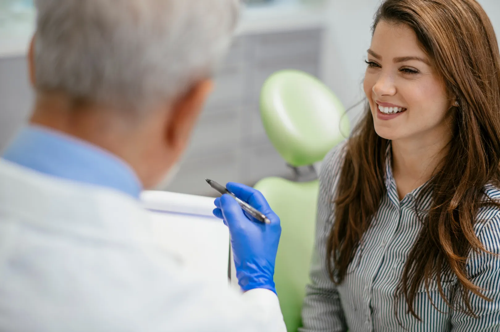 Smiling woman speaking with a healthcare professional wearing blue gloves, holding a pen.