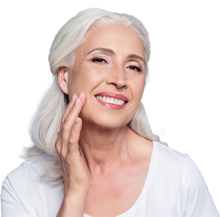 Smiling elderly woman with white hair touching her cheek, wearing a white shirt.