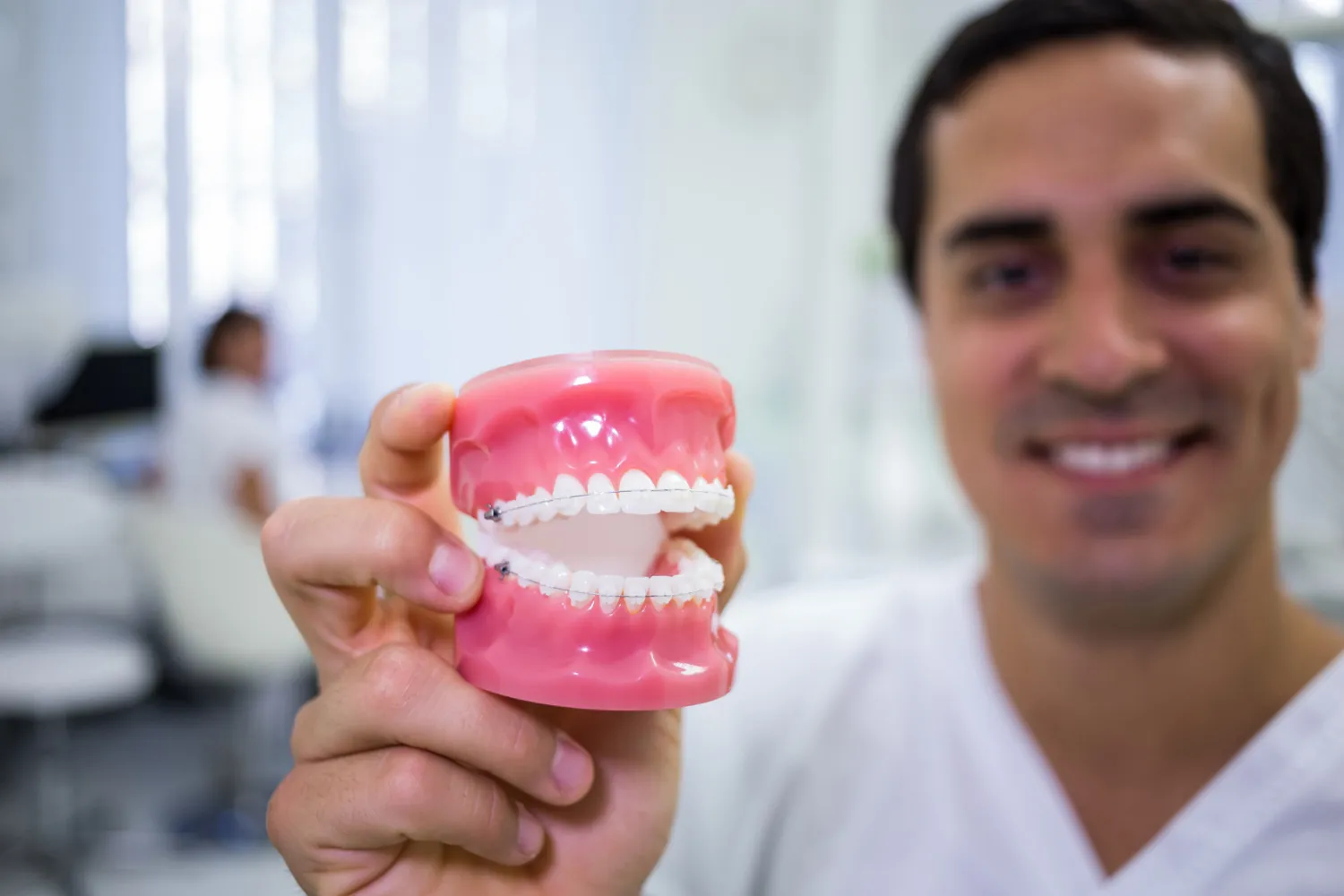 Smiling dentist holding a dental model with clear braces in a clinic.