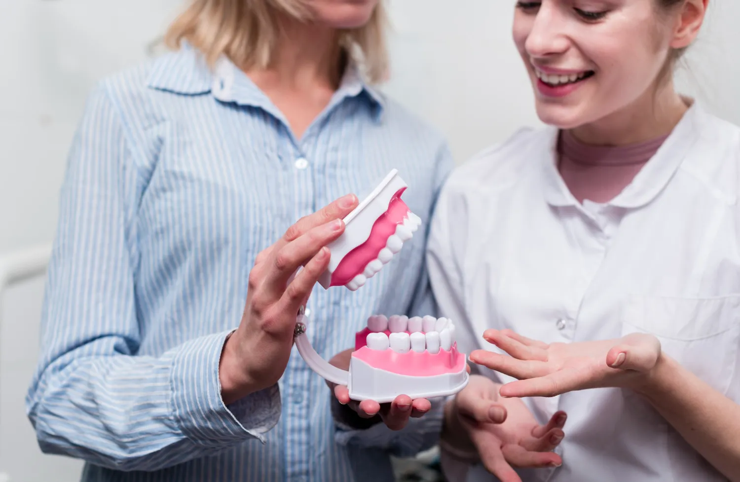 Woman in a striped shirt holding a dental model while a dental professional explains with a smile.
