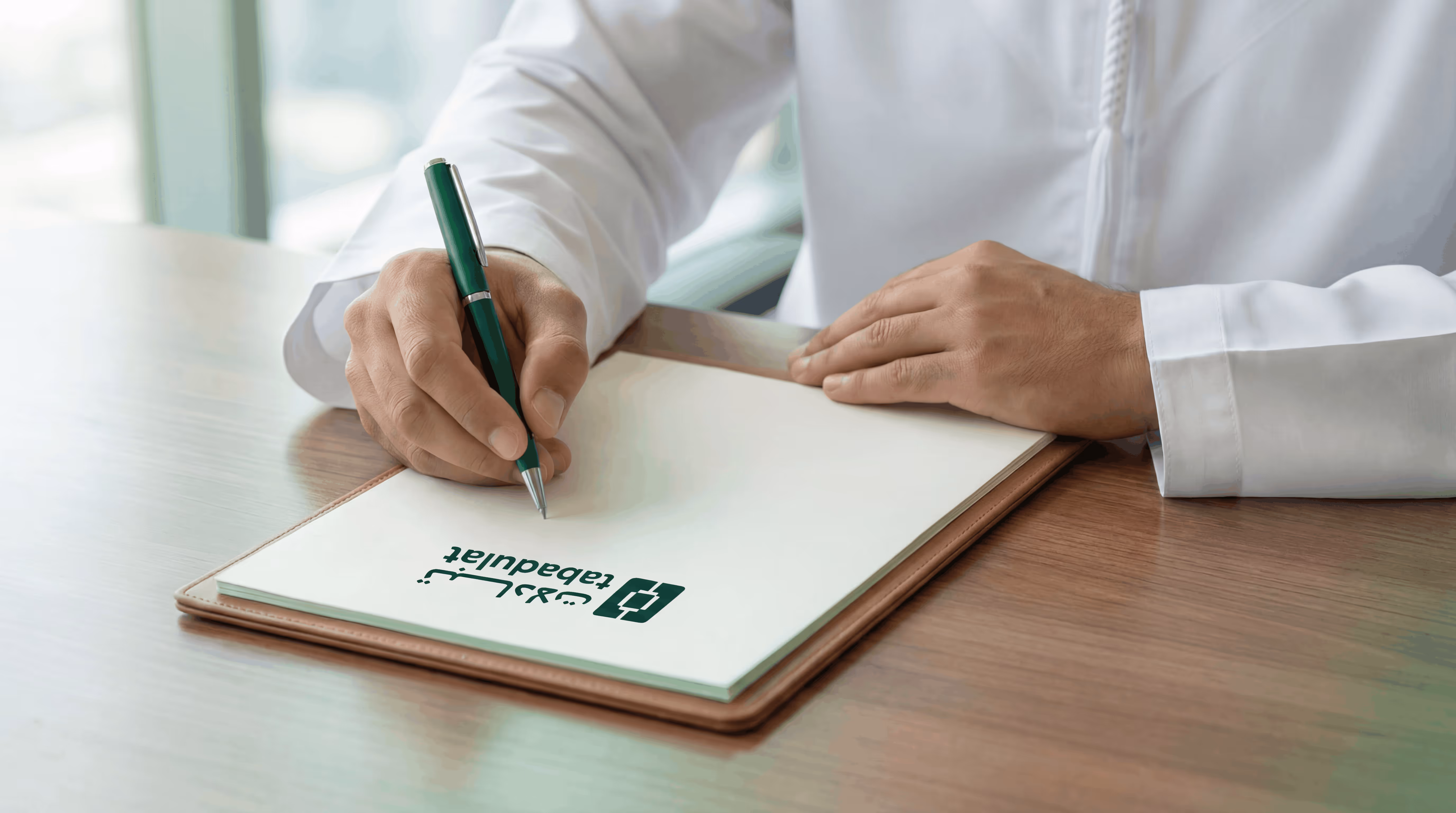 Person wearing white medical attire writing on a clipboard with a pen, paper shows the Tabadulat logo.