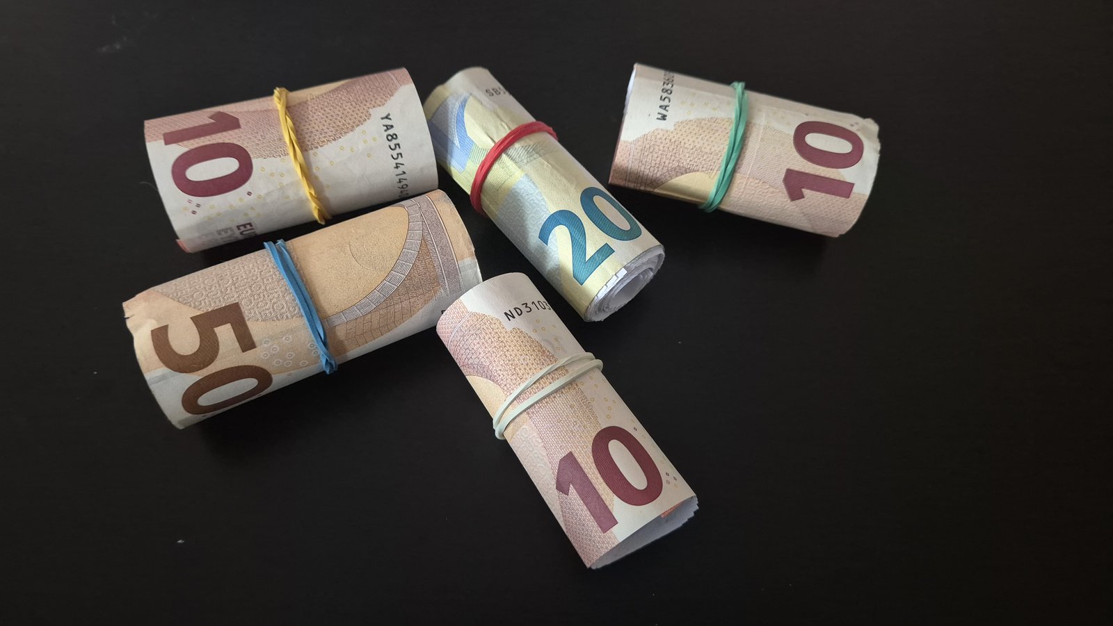 Lažni smotuljci novca: srolani papir omotan novčanicama od 10, 20 i 50 eura, s gumicama, na crnoj podlozi