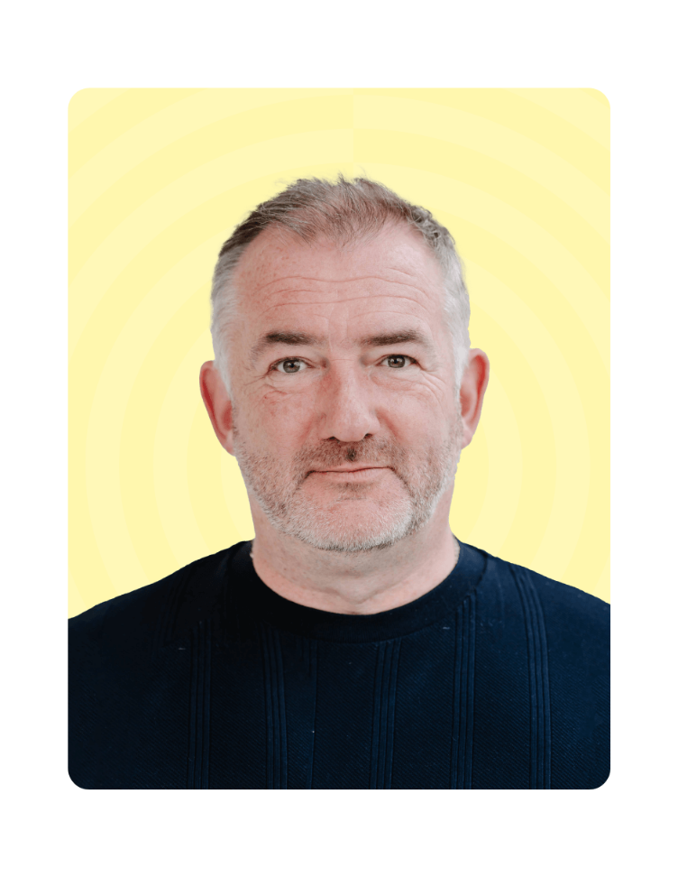Two men shaking hands during a social interaction, one wearing a blue and green patterned scarf and glasses.
