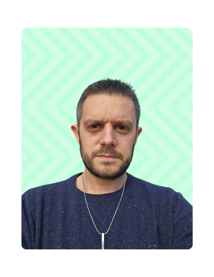 Man with tied-back hair and star tattoo on neck speaking at a microphone while using a laptop on a stand.