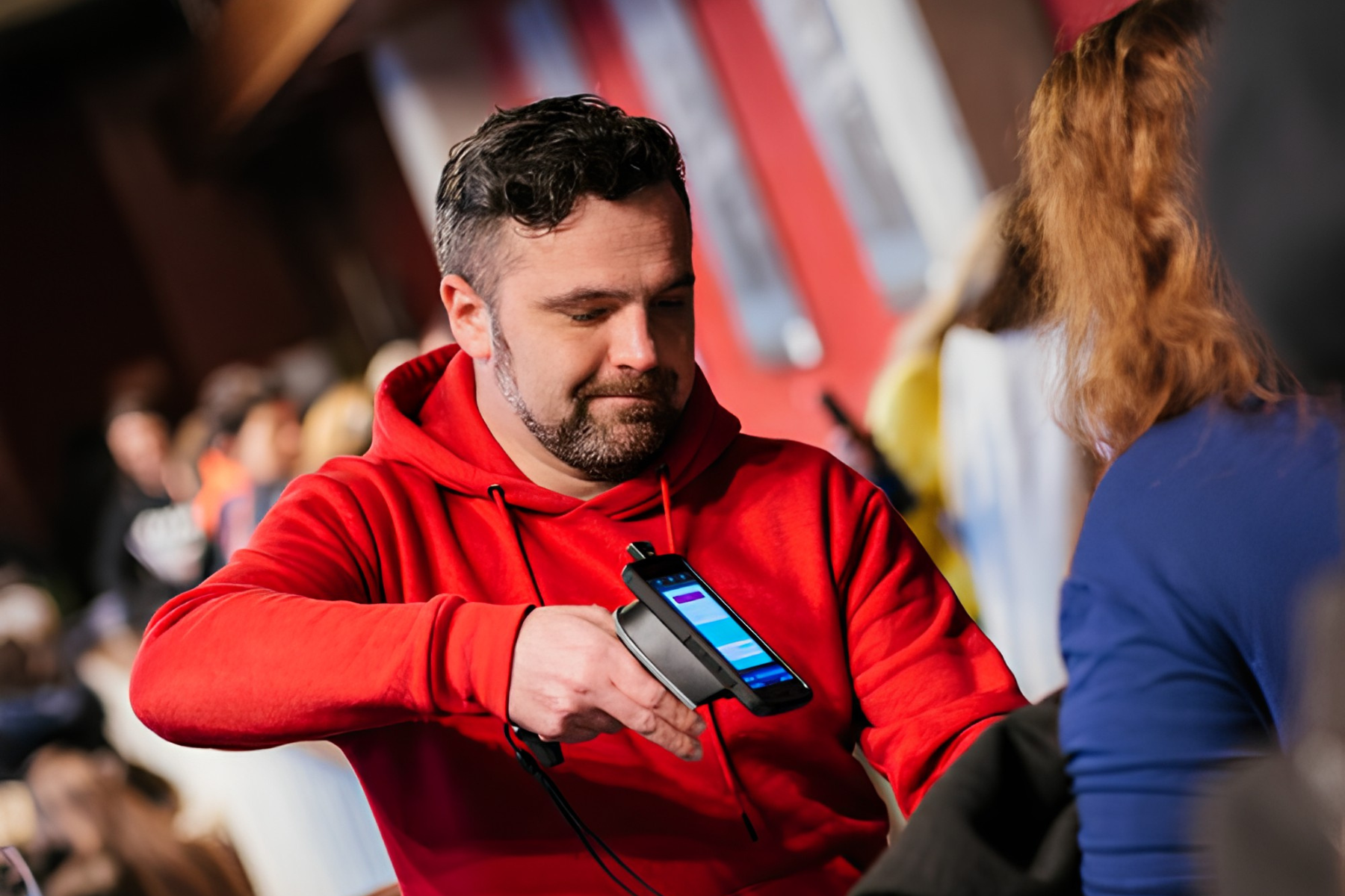 A man and woman wearing conference badges smile and talk while holding mugs, standing in front of a table with pink books and a pink 'ticket' backdrop.