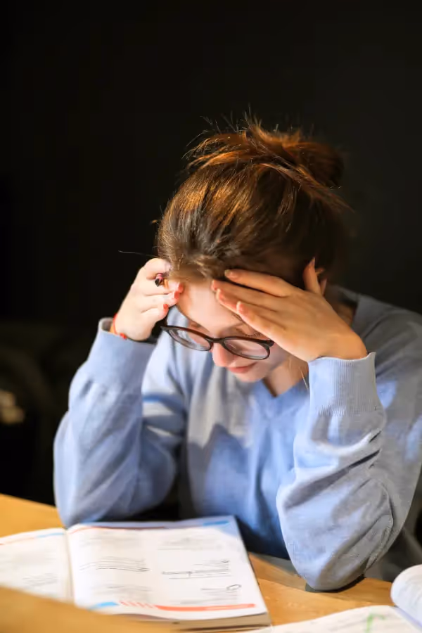 Jovem de óculos sentada com as mãos na cabeça a estudar