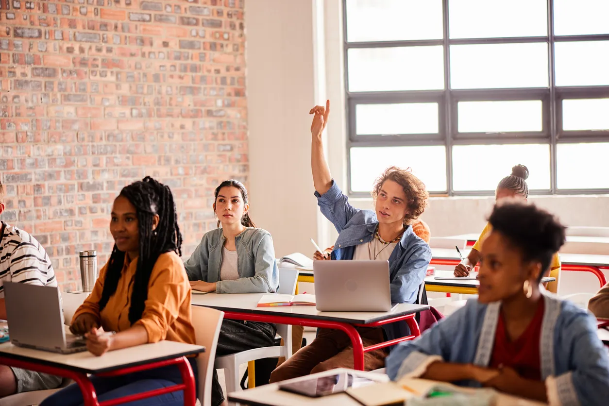 Students at their desk, in a class with their hands raised
