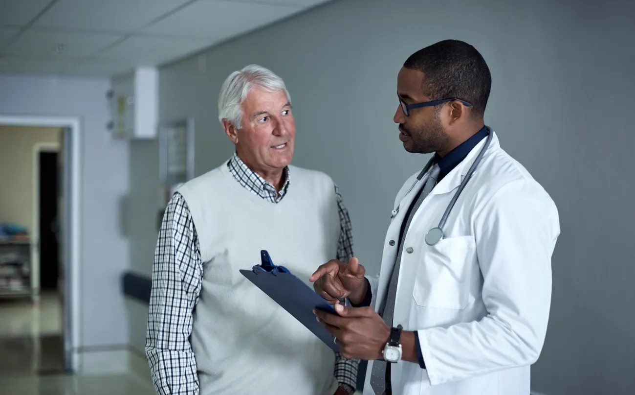 male doctor in a white doctors coat, speaking with older male patient. 