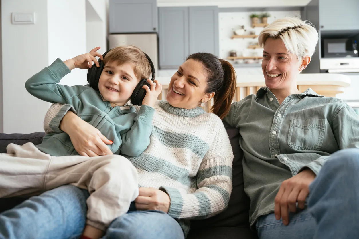 two women, partners, with their child, smiling, sitting on couch