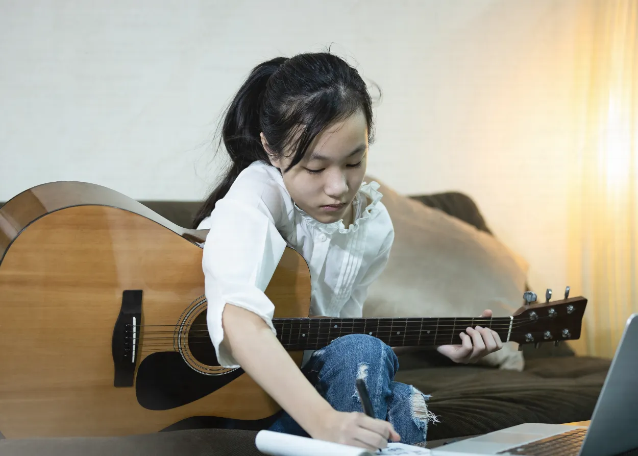 woman playing guitar and writing down notes