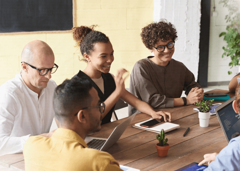 group of people smiling, talking and working at a large table. 