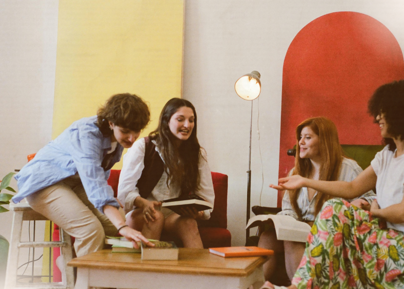 four young people sitting in a colourful living area talking. 