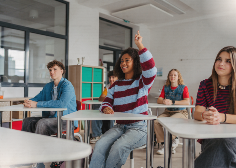 Students in a classroom sitting at their desks, one student raises her hand