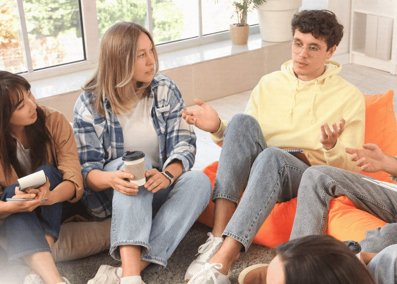 group of people sitting down looking at a young man talking. 
