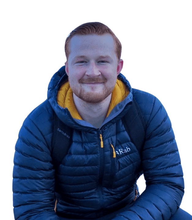 Smiling young man with red hair and beard wearing a blue Rab puffer jacket with a yellow hood lining.
