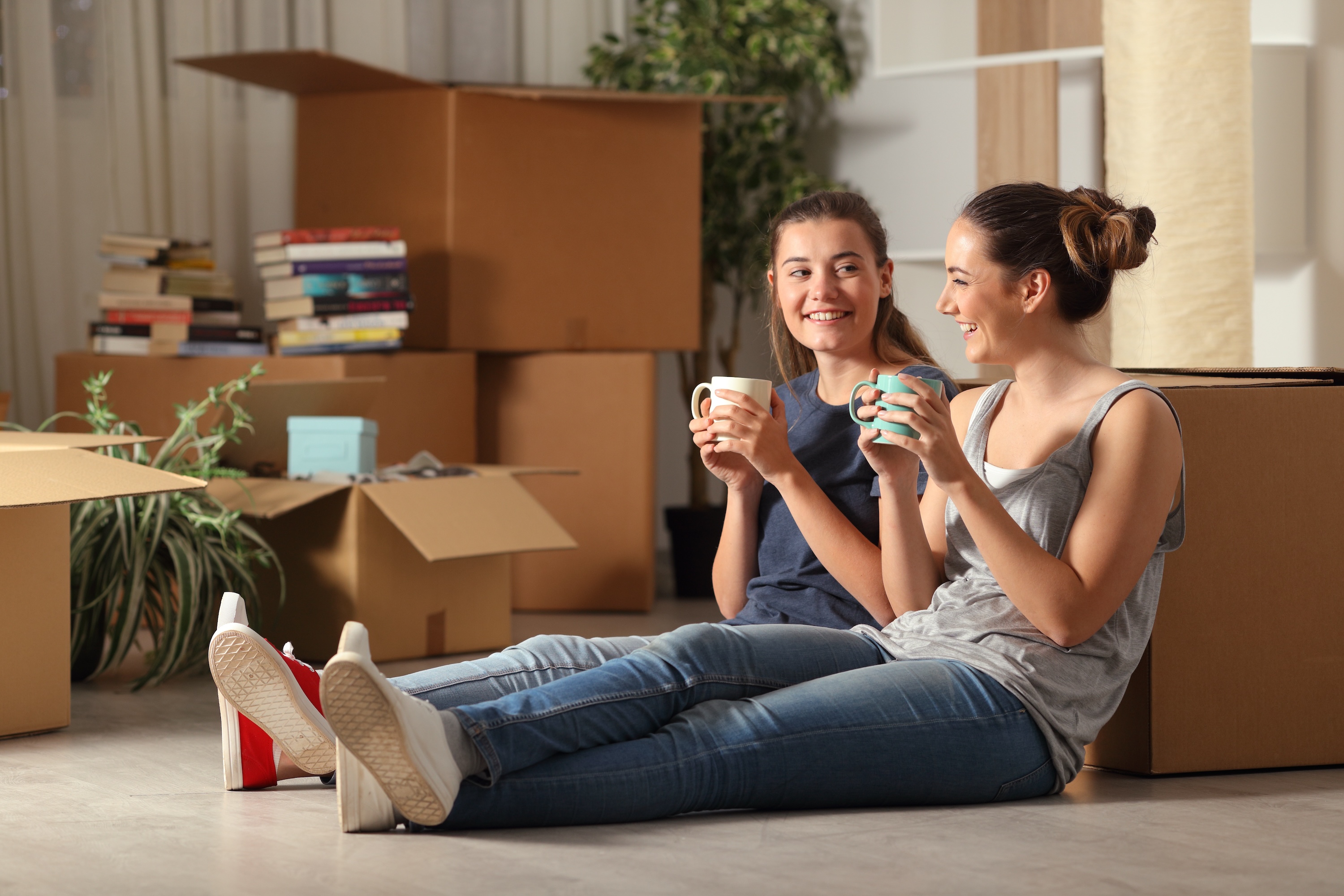 Two female roommates taking a coffee break and smiling amidst moving boxes, symbolizing the seamless move-in experience and cozy atmosphere at ArtHaus Telegraph in Berkeley, CA.
