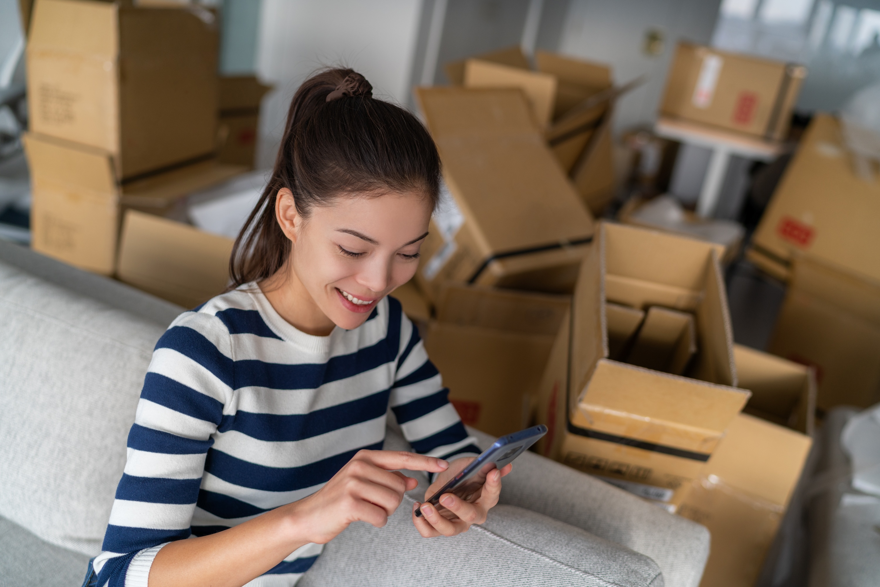 A resident using a smartphone surrounded by moving boxes at ArtHaus Telegraph in Berkeley, CA.