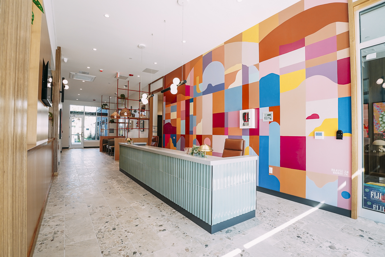 Colorful and modern apartment reception area with a green, ribbed desk and a large abstract geometric mural on the wall at ArtHaus Telegraph in Berkeley, CA.