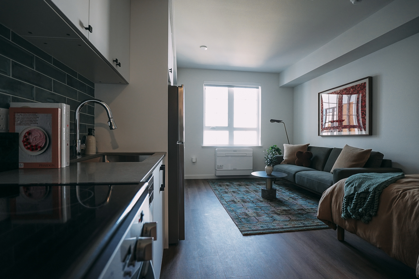 Modern apartment kitchen and living area with two-tone cabinetry (purple and gray), a full-size refrigerator, and large windows at ArtHaus Telegraph in Berkeley, CA.