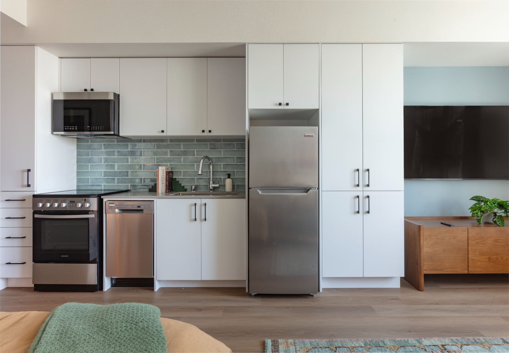 Modern apartment kitchen and living area with two-tone cabinetry (purple and gray), a full-size refrigerator, and large windows at ArtHaus Telegraph in Berkeley, CA.