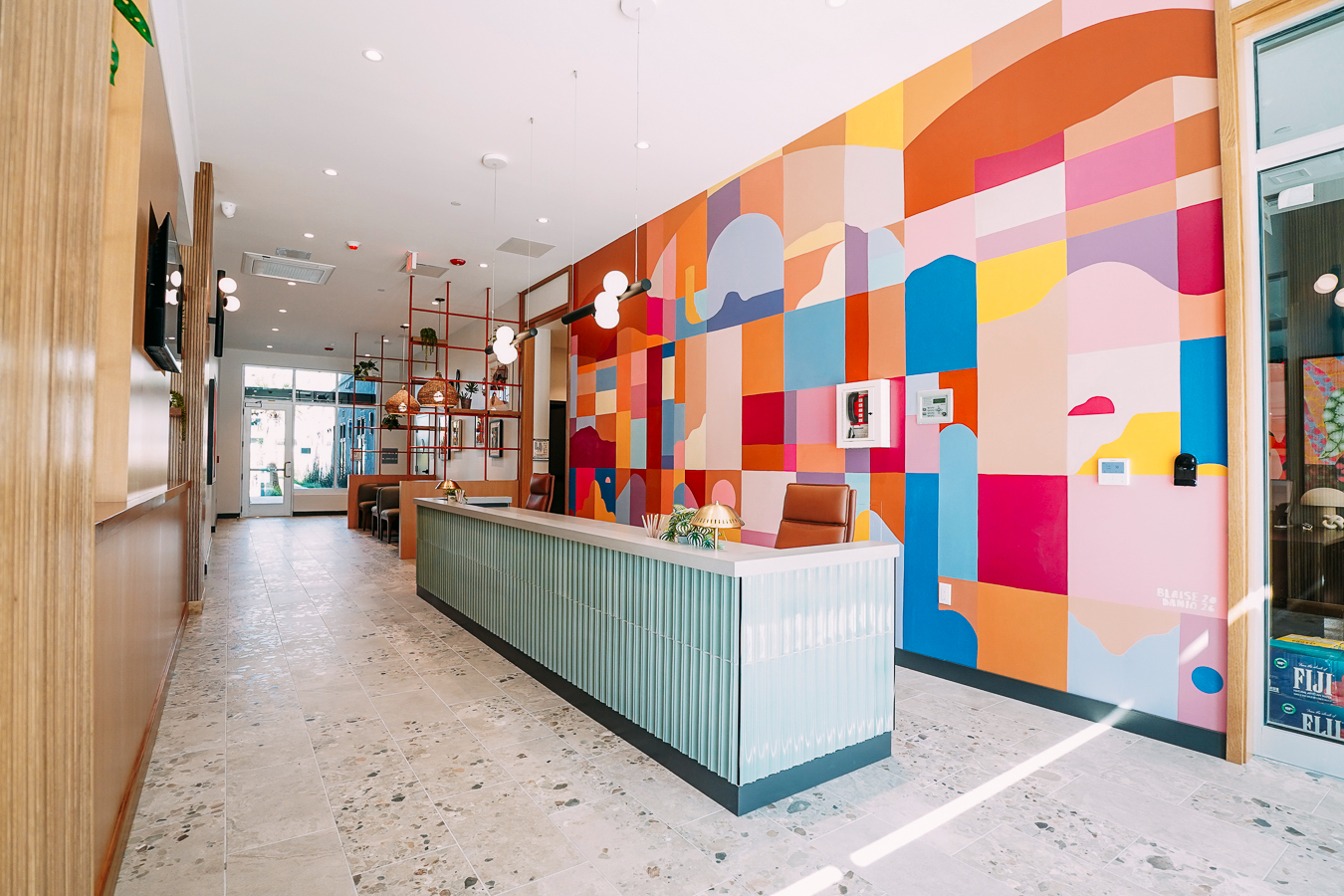 Colorful and modern apartment reception area with a green, ribbed desk and a large abstract geometric mural on the wall at ArtHaus Telegraph in Berkeley, CA.