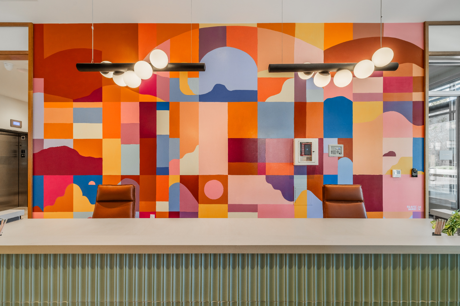 Colorful and modern apartment reception area with a green, ribbed desk and a large abstract geometric mural on the wall at ArtHaus Telegraph in Berkeley, CA.