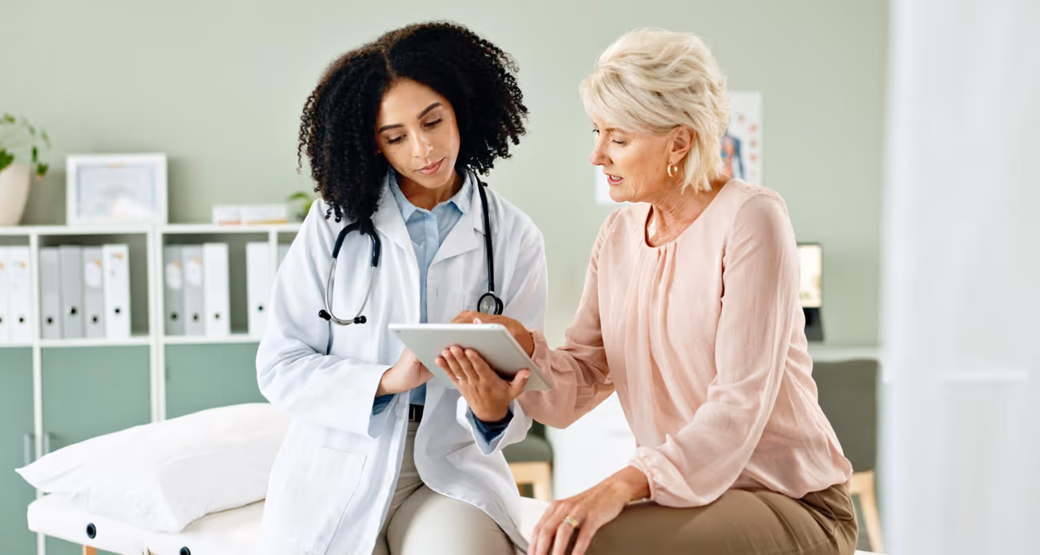 Best concierge doctor in Great Neck, NY, reviewing medical results on a digital tablet with a senior female patient in a modern exam room.