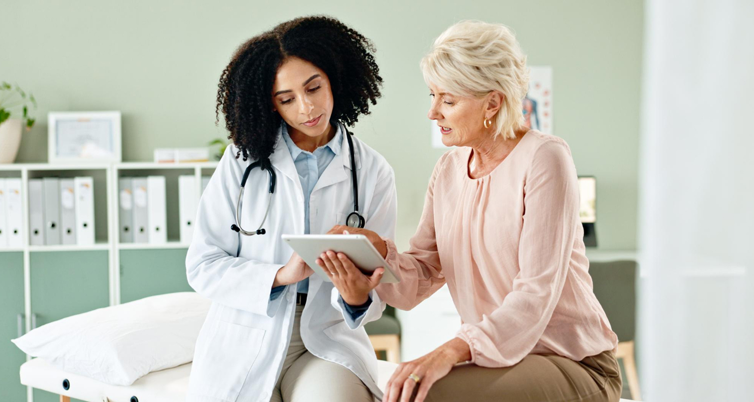 Best concierge doctor in Great Neck, NY, reviewing medical results on a digital tablet with a senior female patient in a modern exam room.