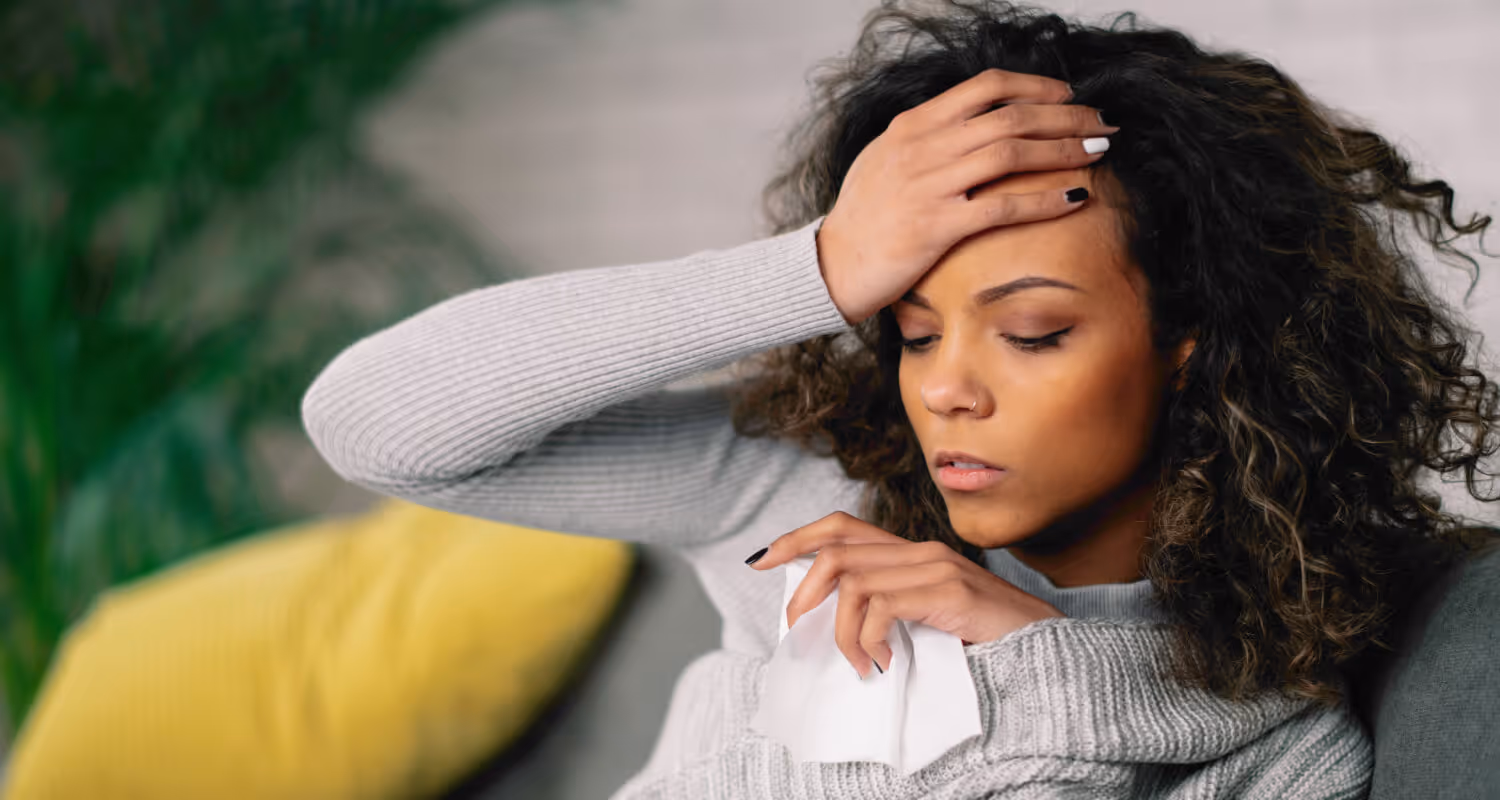 Woman in a gray sweater holding a tissue looks unwell and needs a same-day appointment with a concierge doctor in Great Neck.