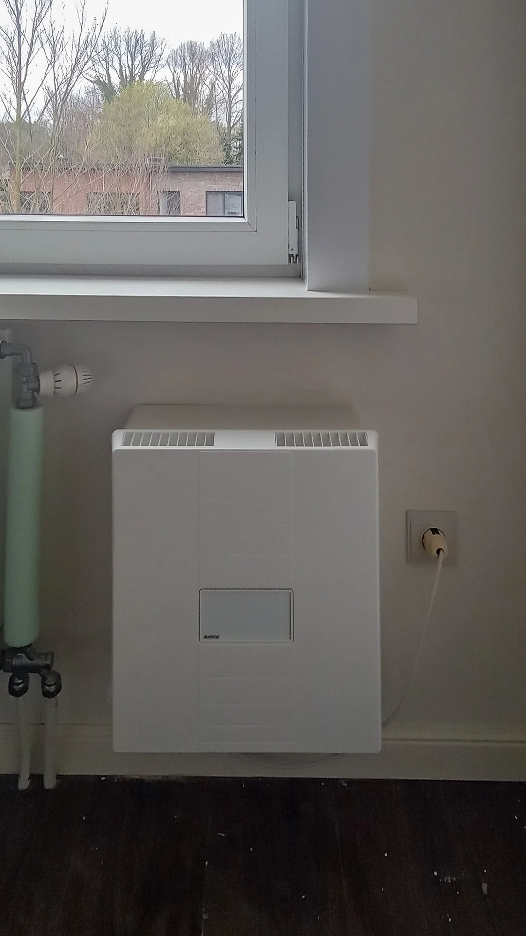 Meltem-ventilatie-unit aan de wand naast de radiator in de eerste kamer