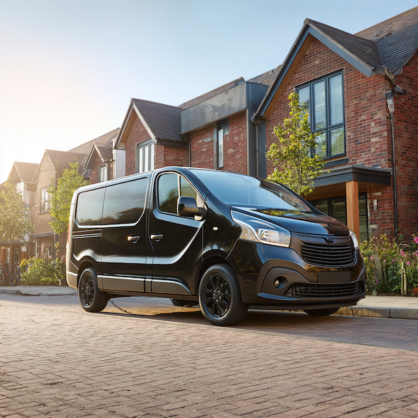Black cargo van parked on a residential street in front of modern brick houses with trees.